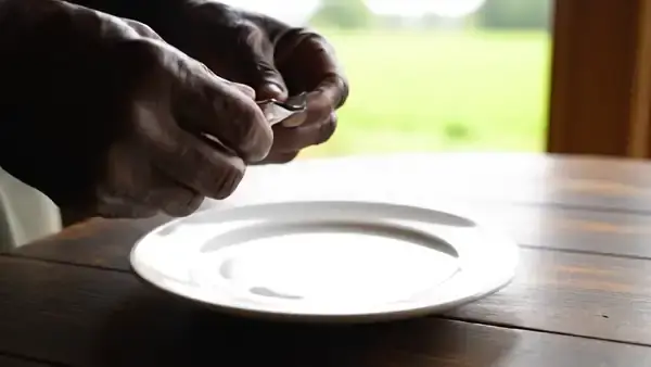 A man's hands tearing a foil packet and spreading seven capsules and a softgel apart on a white plate to count them